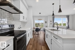 Modern kitchen featuring white cabinetry, quartz countertops, a subway tile backsplash, stainless steel appliances, and wood-finish flooring - 