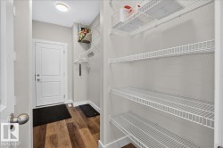 Utility space featuring extensive wire shelving, wood-finish flooring, a white paneled door, and neutral wall paint - 