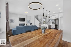Open-concept interior featuring wood-finish flooring, a contemporary kitchen with white shaker cabinetry, stainless steel appliances, and a central island with bar seating - 