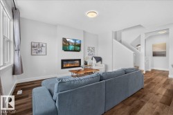 Open-concept living area featuring wood-finish flooring, a contemporary built-in fireplace, recessed ceiling lighting, and a window with trim - 