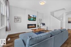 Bright living area featuring a modern linear electric fireplace, wood-finish flooring, white baseboards, and a window with curtains - 