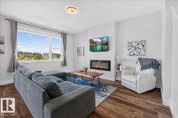Spacious living area featuring expansive windows, wood-finish flooring, a contemporary electric fireplace, and recessed wall space for a television - 