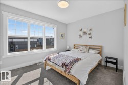 Bedroom featuring a large multi-pane window with white trim, light gray painted walls, and textured gray carpeting - 