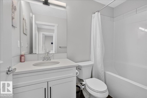 Bathroom featuring a white vanity with an undermount sink, a large mirror, a shower-tub combination with white subway tile surround, and dark flooring - 3805 Cherry Loop Sw, Edmonton, AB - Indoor Photo Showing Bathroom