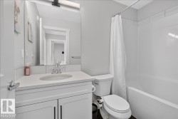 Bathroom featuring a white vanity with an undermount sink, a large mirror, a shower-tub combination with white subway tile surround, and dark flooring - 
