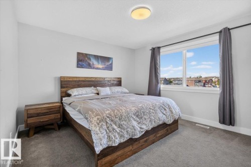 Bright bedroom featuring a large window with white trim, light gray walls, and gray carpet - 3805 Cherry Loop Sw, Edmonton, AB - Indoor Photo Showing Bedroom
