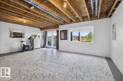 Spacious room featuring patterned flooring, white walls, exposed ceiling joists, and a large window with natural light - 