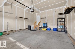 Spacious two-car garage featuring a concrete floor, an overhead garage door mechanism, and a side entry door with a wood staircase - 