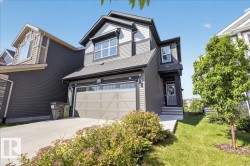 Contemporary two-story exterior featuring a two-tone siding facade, an attached garage with a panel door, a concrete driveway, a front entry with a covered porch, and landscaped greenery - 