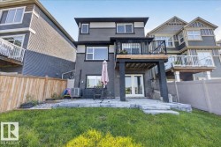 Rear exterior featuring a black wood-finish deck with black railings, a ground-level patio with light-toned pavers, and a manicured lawn - 