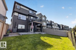 Rear exterior featuring a spacious lawn, a ground-level patio, and an upper-level balcony - 