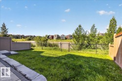 Grassed backyard featuring a paver patio with concrete block retaining wall, private fencing, chain-link perimeter fencing, and a water feature beyond - 