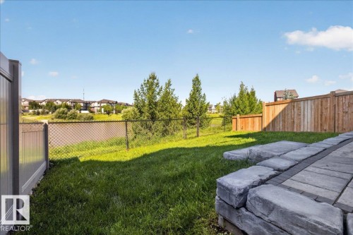Expansive backyard featuring a stone paver patio, lush green lawn, and mature trees - 3805 Cherry Loop Sw, Edmonton, AB - Outdoor