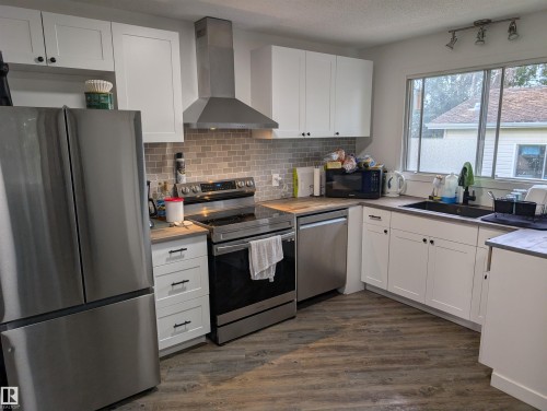 Kitchen featuring white shaker-style cabinetry, wood-finish countertops, stainless steel appliances, a tile backsplash, and wood-finish flooring - 14228 22 Street Nw, Edmonton, AB - Indoor Photo Showing Kitchen With Double Sink
