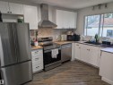 Kitchen featuring white shaker-style cabinetry, wood-finish countertops, stainless steel appliances, a tile backsplash, and wood-finish flooring - 14228 22 Street Nw, Edmonton, AB  - Indoor Photo Showing Kitchen With Double Sink 