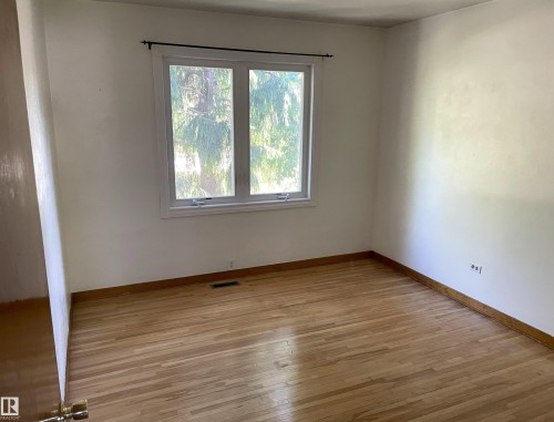 Bright room featuring wood-finish flooring, white walls, and a large window with a black curtain rod - 11308 73 Avenue Nw, Edmonton, AB - Indoor Photo Showing Other Room