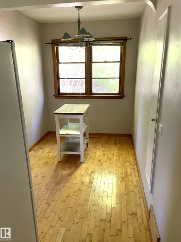 Bright room featuring wood-finish flooring, a double window with wood trim, and a three-light chandelier - 11308 73 Avenue Nw, Edmonton, AB - Indoor Photo Showing Other Room