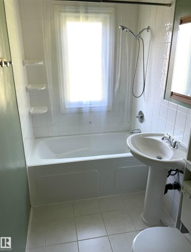 Bathroom featuring a pedestal sink with chrome fixtures, a full-size bathtub with an integrated shower, and white ceramic tile flooring - 11308 73 Avenue Nw, Edmonton, AB - Indoor Photo Showing Bathroom