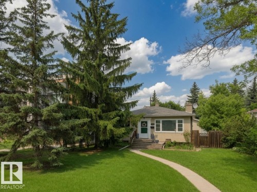 Single-story residence featuring a concrete walkway, mature evergreen trees, and a manicured lawn - 11308 73 Avenue Nw, Edmonton, AB - Outdoor