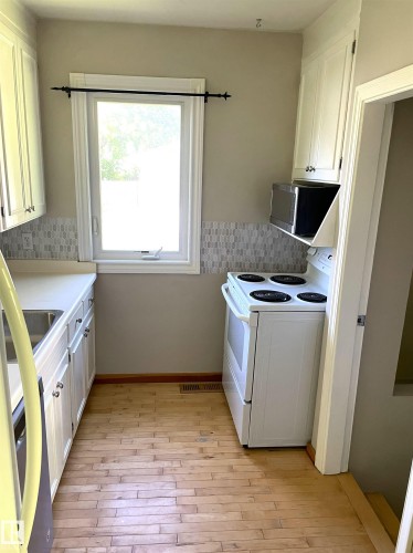 Compact kitchen featuring light wood-finish flooring, white cabinetry with silver-tone hardware, and a white electric range - 11308 73 Avenue Nw, Edmonton, AB - Indoor Photo Showing Kitchen