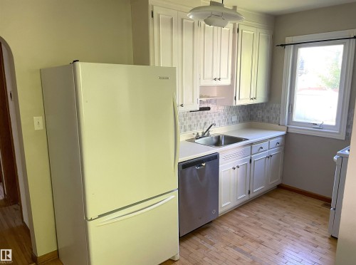 Kitchen featuring white cabinetry, light-toned countertops, tile backsplash, and wood-finish flooring - 11308 73 Avenue Nw, Edmonton, AB - Indoor Photo Showing Kitchen
