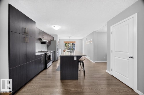 Open-concept kitchen featuring dark wood-finish cabinetry, stainless steel appliances, and a central island with countertop seating - 3043 Keswick Way Sw, Edmonton, AB - Indoor Photo Showing Other Room