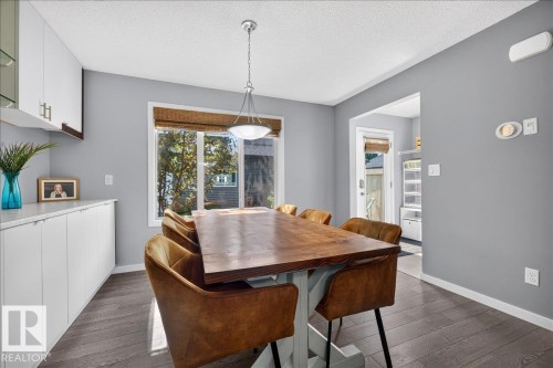 Spacious dining area featuring dark wood-finish flooring, a large window, a ceiling-mounted light fixture, extensive white built-in cabinetry, and light gray walls - 3043 Keswick Way Sw, Edmonton, AB - Indoor Photo Showing Dining Room