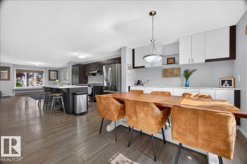 Open-concept living space featuring wood-finish flooring, a kitchen island with seating, dark wood cabinetry, stainless steel appliances, and a dedicated dining area with a contemporary chandelier - 3043 Keswick Way Sw, Edmonton, AB - Indoor