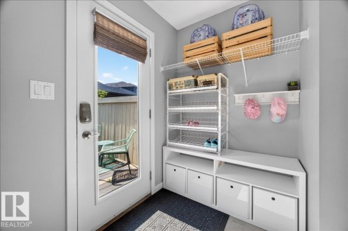 Mudroom featuring built-in white shelving with pull-out drawers, wire rack storage, wall-mounted coat hooks, and an exterior door with integrated blinds - 3043 Keswick Way Sw, Edmonton, AB - Indoor