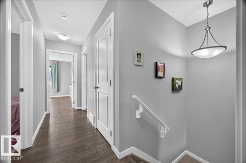 Hallway featuring wood-finish flooring, light grey walls, white trim, and multiple white panel doors - 3043 Keswick Way Sw, Edmonton, AB - Indoor Photo Showing Other Room