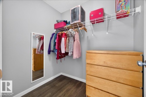 Walk-in closet with dark wood-finish flooring, light grey walls, white baseboards, and a wire shelving system with hanging rod - 3043 Keswick Way Sw, Edmonton, AB - Indoor With Storage