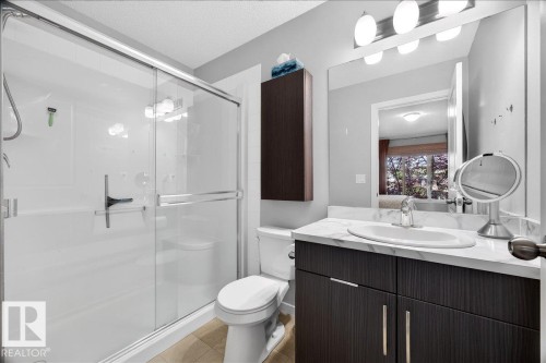 Full bathroom featuring a shower with sliding glass doors, a vanity with a white countertop and integrated sink, a large wall-mounted mirror, and a wall-mounted storage cabinet - 3043 Keswick Way Sw, Edmonton, AB - Indoor Photo Showing Bathroom