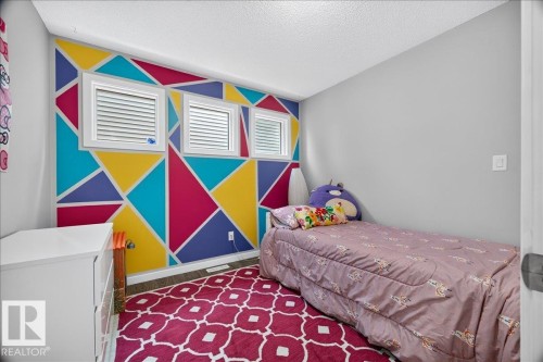 Accent wall with geometric pattern, multiple windows with blinds, light gray wall finish, wood-finish flooring, and white trim - 3043 Keswick Way Sw, Edmonton, AB - Indoor Photo Showing Bedroom