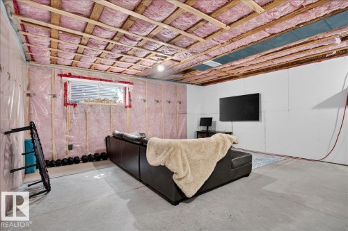Lower level space featuring exposed ceiling joists with insulation, a window with horizontal blinds, and a partial drywall finish on one wall - 3043 Keswick Way Sw, Edmonton, AB - Indoor Photo Showing Basement