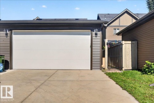 Attached garage with a white overhead door, dark trim, and two exterior wall sconces - 3043 Keswick Way Sw, Edmonton, AB - Outdoor With Exterior