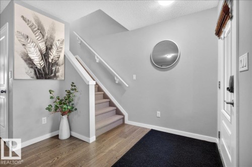 Entryway featuring wood-finish flooring, a carpeted staircase with white railings, and light grey wall paint - 3043 Keswick Way Sw, Edmonton, AB - Indoor Photo Showing Other Room
