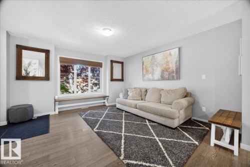 Spacious interior featuring wood-finish flooring, a large window with a built-in bench, and neutral wall tones - 3043 Keswick Way Sw, Edmonton, AB - Indoor Photo Showing Living Room