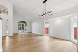 Spacious living area featuring light wood-finish flooring, vaulted ceilings, and white painted walls - 