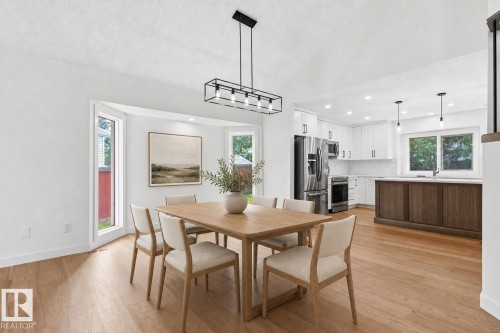 Open-concept dining area featuring light wood-finish flooring and a contemporary linear chandelier - 140 Healy Road Nw, Edmonton, AB - Indoor Photo Showing Dining Room