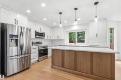Modern kitchen featuring white cabinetry, stainless steel appliances, a center island with wood-finish paneling, light wood-finish flooring, and recessed ceiling lighting - 