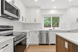 Contemporary kitchen featuring white shaker cabinetry, stainless steel appliances, light countertops, and wood-finish flooring - 