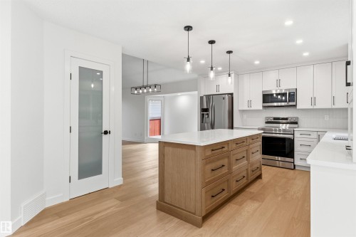 Modern kitchen featuring a light wood-finish island with integrated storage, white perimeter cabinetry, stainless steel appliances, and white countertops - 140 Healy Road Nw, Edmonton, AB - Indoor Photo Showing Kitchen With Upgraded Kitchen