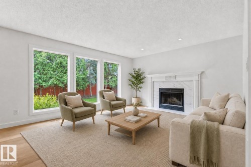 Light-filled living area featuring three large windows, a marble-surround fireplace with a white mantel, recessed lighting, and wood-finish flooring - 140 Healy Road Nw, Edmonton, AB - Indoor Photo Showing Living Room With Fireplace