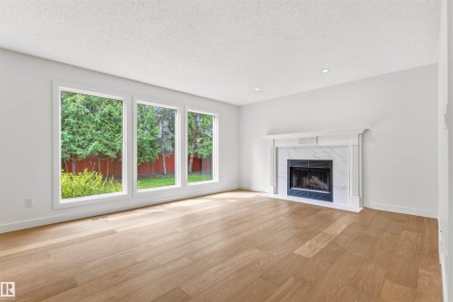 Spacious room with light wood-finish flooring, three large windows, and recessed lighting - 140 Healy Road Nw, Edmonton, AB - Indoor Photo Showing Living Room With Fireplace
