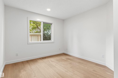 Bright interior room featuring a window with exterior views, wood-finish flooring, white walls, recessed ceiling lighting, and white baseboards - 140 Healy Road Nw, Edmonton, AB - Indoor Photo Showing Other Room