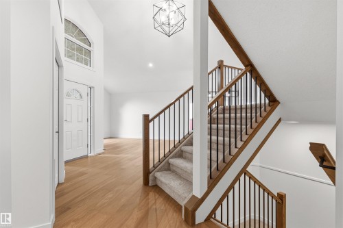 Two-story entryway with a decorative front door, arched transom window, wood-finish flooring, and a staircase featuring wood handrails and black metal balusters - 140 Healy Road Nw, Edmonton, AB - Indoor Photo Showing Other Room