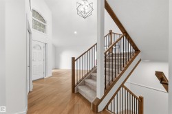 Two-story entryway with a decorative front door, arched transom window, wood-finish flooring, and a staircase featuring wood handrails and black metal balusters - 