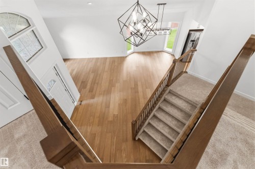 Foyer and living space featuring a carpeted staircase with wood railings, a modern geometric chandelier, and wood-finish flooring - 140 Healy Road Nw, Edmonton, AB - Indoor Photo Showing Other Room