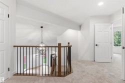 Upper landing featuring neutral carpet flooring, white walls, and a modern geometric chandelier - 