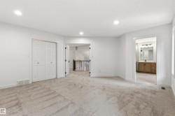 Spacious carpeted room featuring recessed lighting, a bi-fold closet, and access to a full bathroom with a wood-finish vanity - 